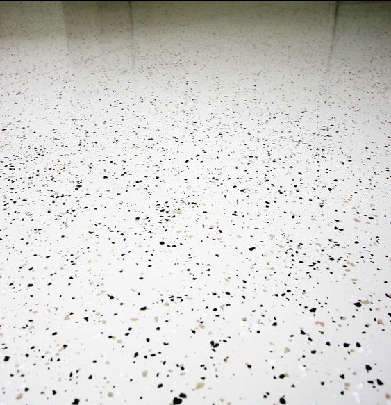 Biała posadzka przemysłowa z czarnymi i beżowymi drobnymi plamkami, widoczny połysk i odbicie światła.