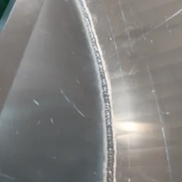 Detal spoiny na metalowej powierzchni z widocznymi śladami szlifowania i rysami.