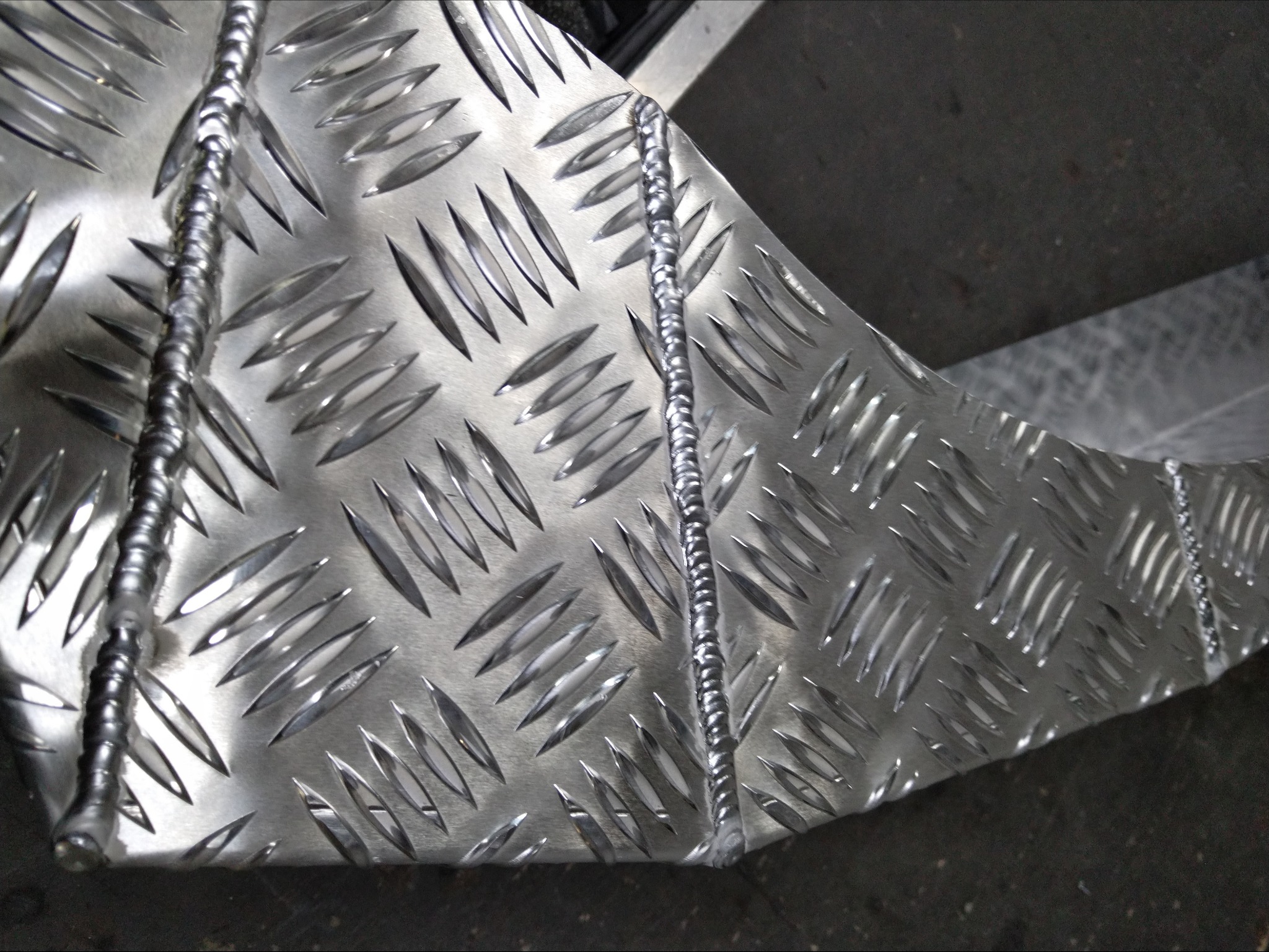 Fragment metalowej konstrukcji z wyraźnym wzorem łezkowym, połączonej grubym spoiwem spawalniczym.