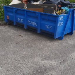 Firma Sprzątająca Blask - Niebieski kontener PUK Rumia wypełniony odpadami poremontowymi i meblami, widoczne płyty meblowe, fragment sofy i worki na śmieci.