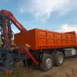 Pomarańczowa wywrotka z dźwigiem VKRANE zaparkowana na placu budowy, widoczna z boku, z otwartymi drzwiami kabiny.