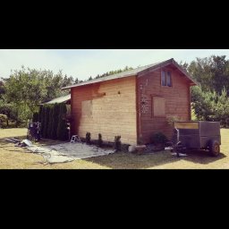 Firma usługowa Kacper Juskowiak - Drewniany domek letniskowy z przyczepką na trawniku, przygotowany do prac malarskich, z widoczną plandeką, narzędziami i drabinką.