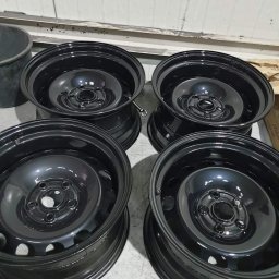 Firma usługowa Kacper Juskowiak - Cztery czarne, metalowe felgi samochodowe po renowacji z Kruszwicy, ustawione na szarej podłodze w warsztacie.