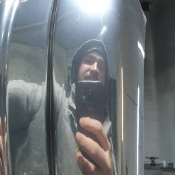 Firma usługowa Kacper Juskowiak - Osoba robiąca selfie w odbiciu wypolerowanego elementu metalowego, prawdopodobnie po procesie obróbki, widoczne niewielkie niedoskonałości na powierzchni.