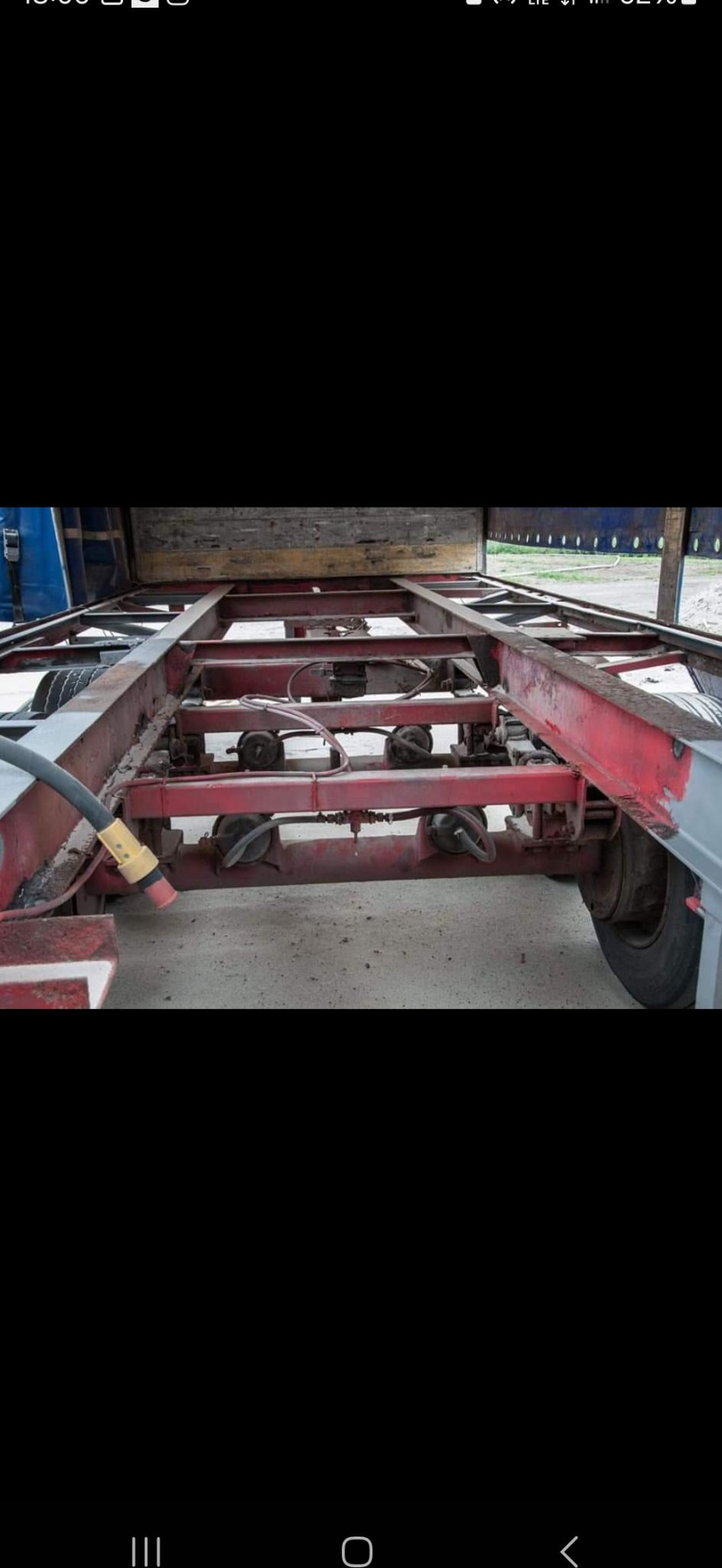 Podwozie przyczepy lawety z widocznymi elementami konstrukcyjnymi, pneumatyką i śladami użytkowania, częściowo pomalowane na czerwono i szaro.