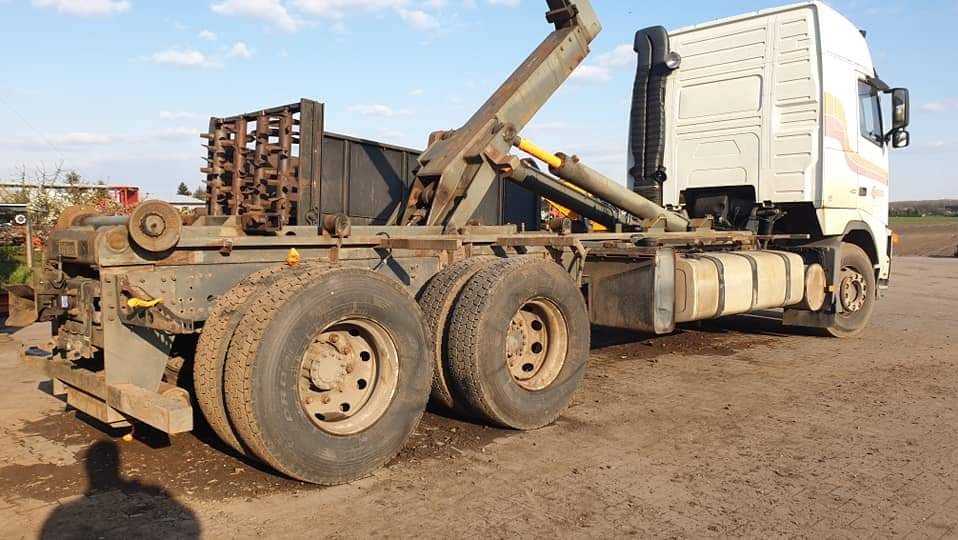 Ciężarówka z hydraulicznym dźwigiem kontenerowym, widok z boku na brudnym placu w słoneczny dzień.