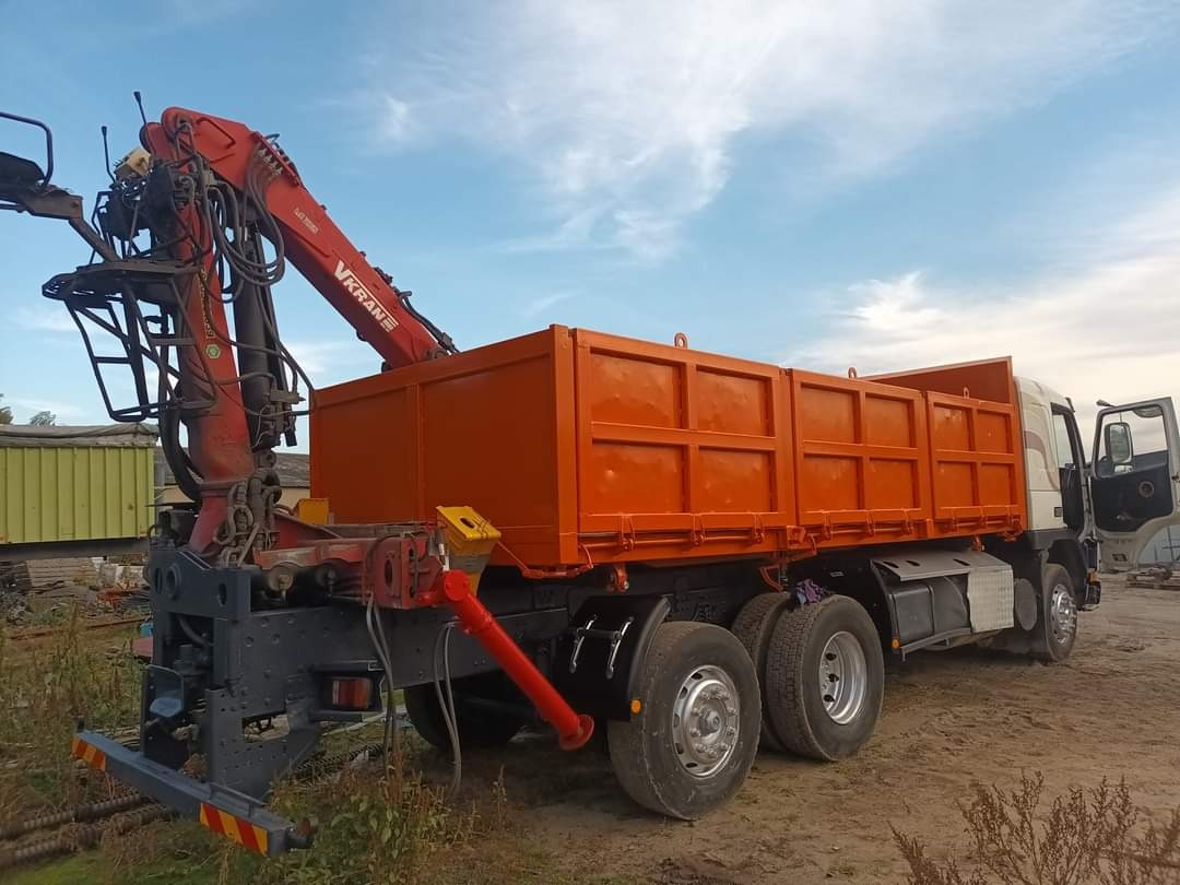 Pomarańczowa wywrotka z dźwigiem VKRANE zaparkowana na placu budowy, widoczna z boku, z otwartymi drzwiami kabiny.