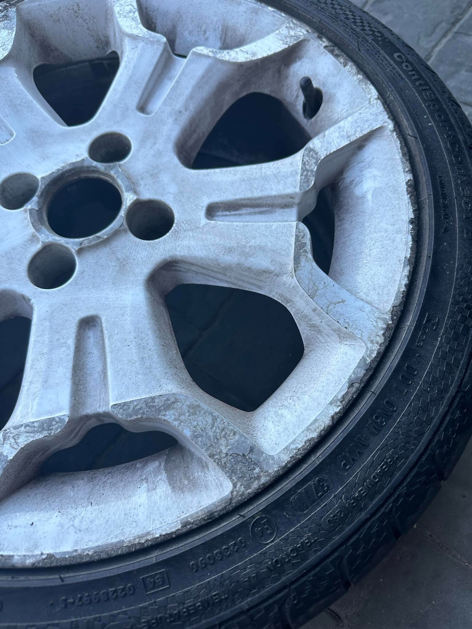 Brudna felga aluminiowa z oponą, widoczne ślady użytkowania i zabrudzenia na powierzchni, z bliska.