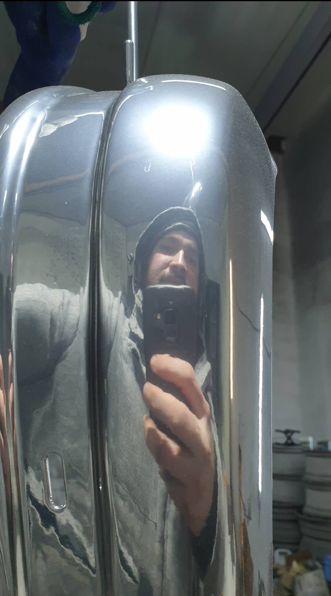 Osoba robiąca selfie w odbiciu wypolerowanego elementu metalowego, prawdopodobnie po procesie obróbki, widoczne niewielkie niedoskonałości na powierzchni.