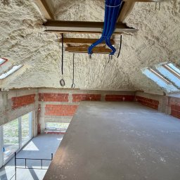 RAF - Development Rafał Kościuk - Poddasze po ociepleniu pianką PUR, widoczne okna dachowe i niebieskie rury wentylacyjne. Ściany z czerwonej cegły częściowo otynkowane. Surowe wykończenie.