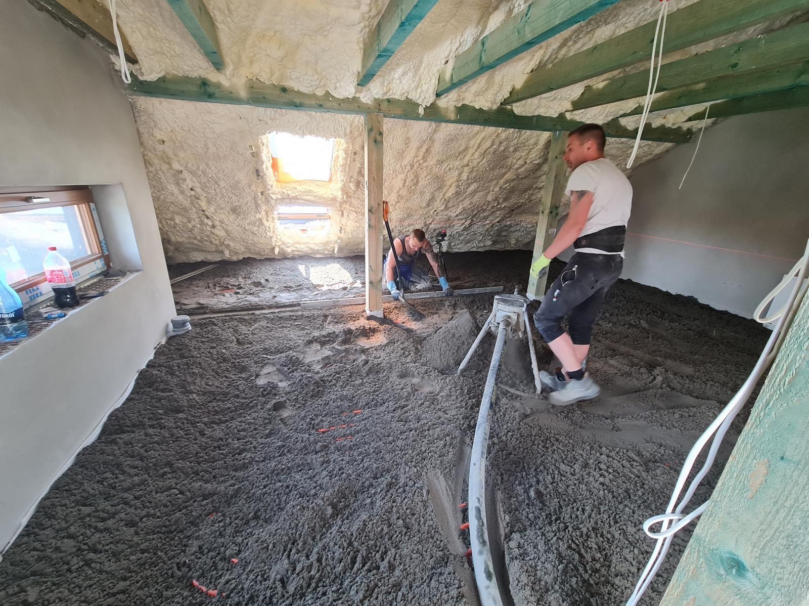 Prace w trakcie w Obornikach Śląskich: w pomieszczeniu na poddaszu, po ociepleniu pianką, dwóch mężczyzn rozprowadza wylewkę cementową, używając poziomicy i listwy wibracyjnej.