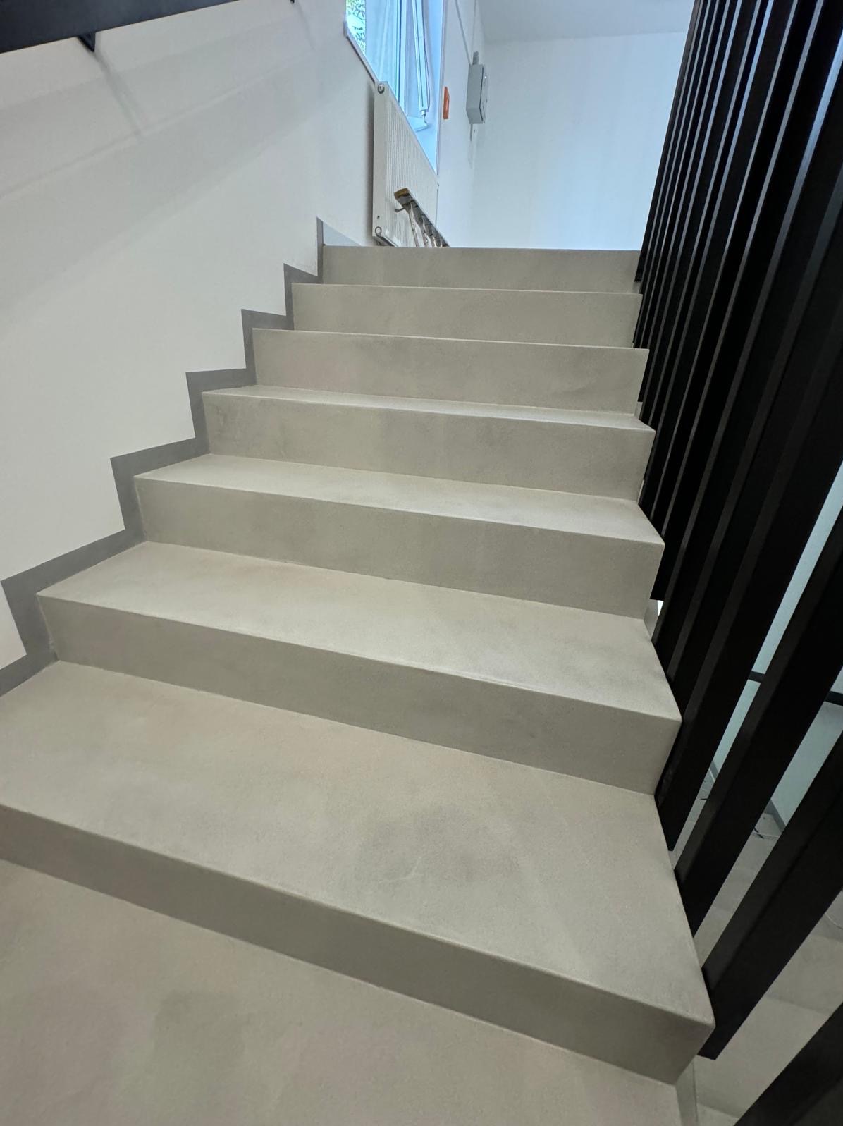 Schody wewnętrzne wykończone jasnoszarym tynkiem dekoracyjnym, z czarną balustradą z pionowych listew.