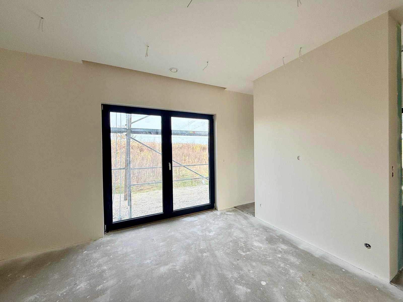 Wnętrze po gładziowaniu ścian, z widocznymi śladami prac na podłodze i oknem balkonowym z czarną ramą. Na zewnątrz rusztowanie.