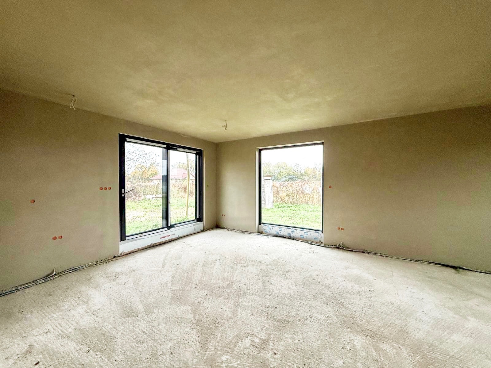 Wnętrze po tynkowaniu w Obornikach Śląskich: ściany pokryte świeżym tynkiem, widoczne okna i instalacje elektryczne. Podłoga surowa, przygotowana do dalszych prac.