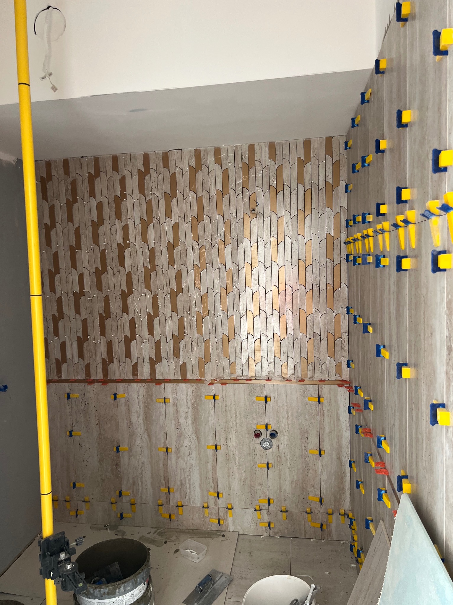 Układanie płytek w łazience z użyciem systemu poziomowania. Częściowo ułożona dekoracyjna mozaika. Widoczne narzędzia glazurnicze.