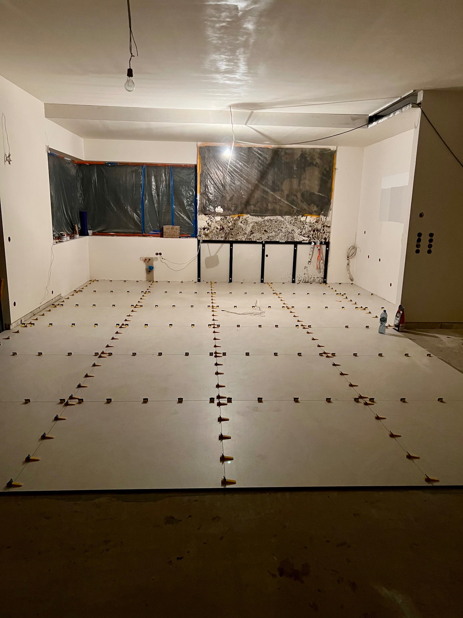 Układanie płytek podłogowych z użyciem systemu poziomowania. Widoczne krzyżyki dystansowe i linki. Ściany przygotowane do dalszych prac wykończeniowych.