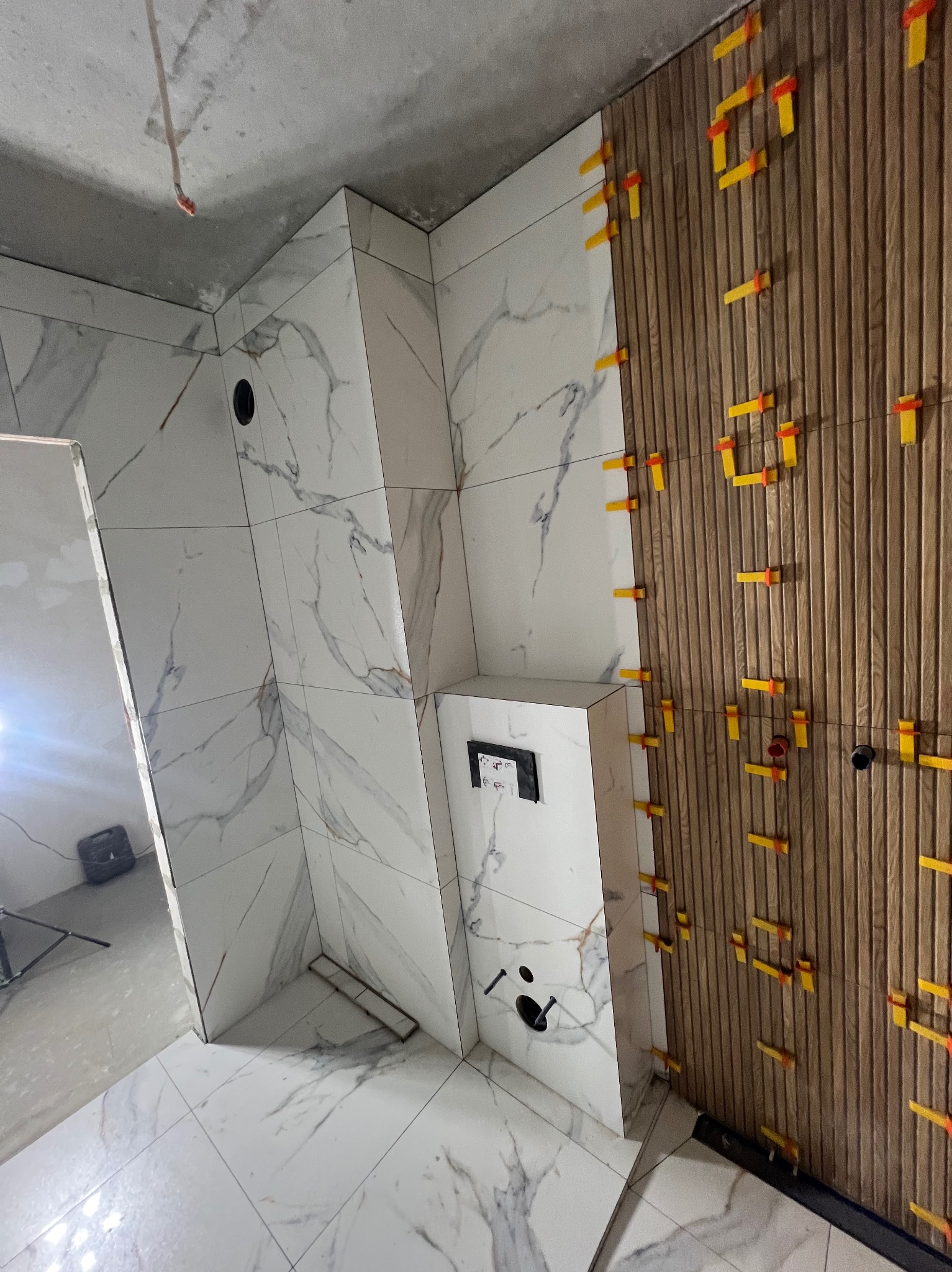 Układanie płytek imitujących drewno i marmur w łazience w Poznaniu. Widoczne klipsy poziomujące. Częściowo wykończona ściana i podłoga.