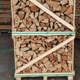 Paleta szczap drewna opałowego, zabezpieczona folią i drewnianą ramą z zielonymi paskami, na tle ściany z desek.