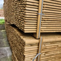 FW ILTRANS SPÓŁKA Z OGRANICZONĄ ODPOWIEDZIALNOŚCIĄ - Stosy równo ułożonych, jasnych, obrzynanych desek, zabezpieczonych szarą taśmą, czekających na transport.