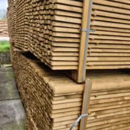 Stosy równo ułożonych, jasnych, obrzynanych desek, zabezpieczonych szarą taśmą, czekających na transport.