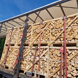 FW ILTRANS SPÓŁKA Z OGRANICZONĄ ODPOWIEDZIALNOŚCIĄ - Załadunek drewna kominkowego w skrzyniach na naczepie, zabezpieczone pasami transportowymi, widok na błękitne niebo.
