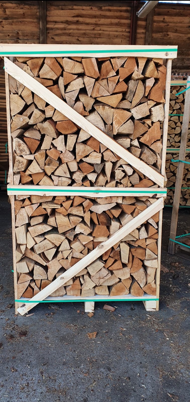 Dwa kosze z ułożonym, pociętym drewnem, zabezpieczone drewnianymi listwami i zieloną taśmą, ustawione jeden na drugim na palecie.