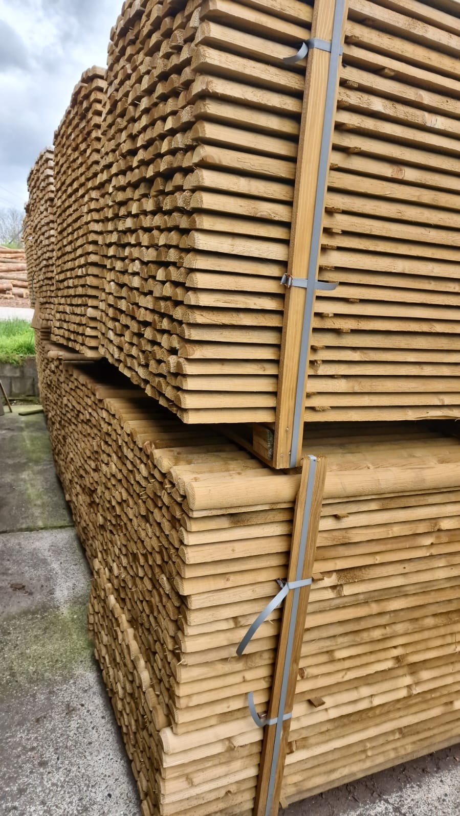 Stosy równo ułożonych, jasnych, obrzynanych desek, zabezpieczonych szarą taśmą, czekających na transport.