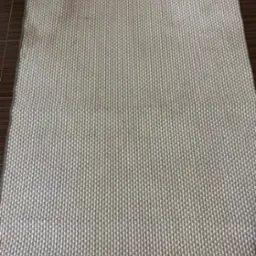 Szaro-biały dywan z geometrycznym wzorem w pionowe prążki, leżący na ciemnobrązowej podłodze z płytek ceramicznych.