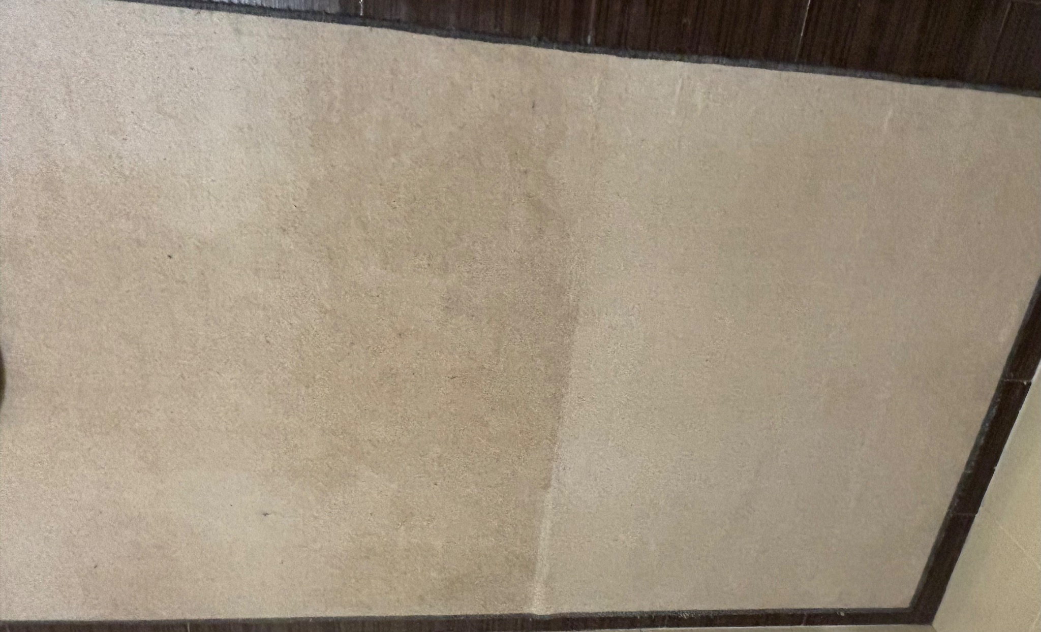 Fragment dywanu z widoczną różnicą w czystości po lewej stronie, kontrastujący z ciemną listwą przypodłogową.