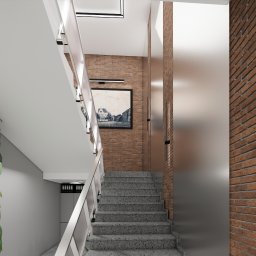 WICZ Interiors design - Klatka schodowa z szarymi schodami, białą balustradą i ceglaną ścianą z obrazem w czarnej ramie, oświetlona lampą LED, z roślinami doniczkowymi po lewej stronie.