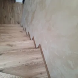 Drewnopodobne panele na schodach z wykończeniem przy ścianie o fakturze dekoracyjnej.