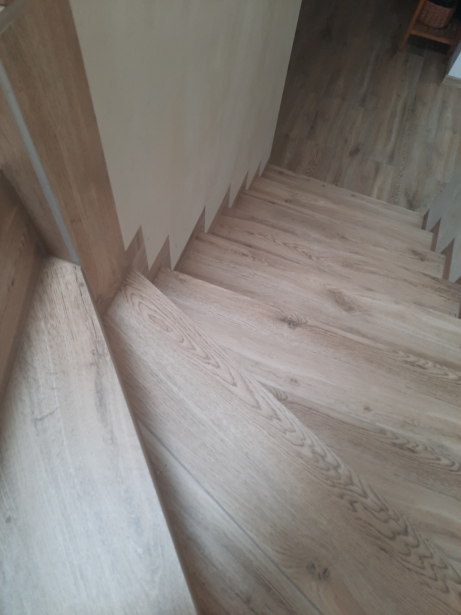 Schody wykończone panelami podłogowymi w odcieniach jasnego drewna, widok z góry na stopnie i fragment ściany w tle.