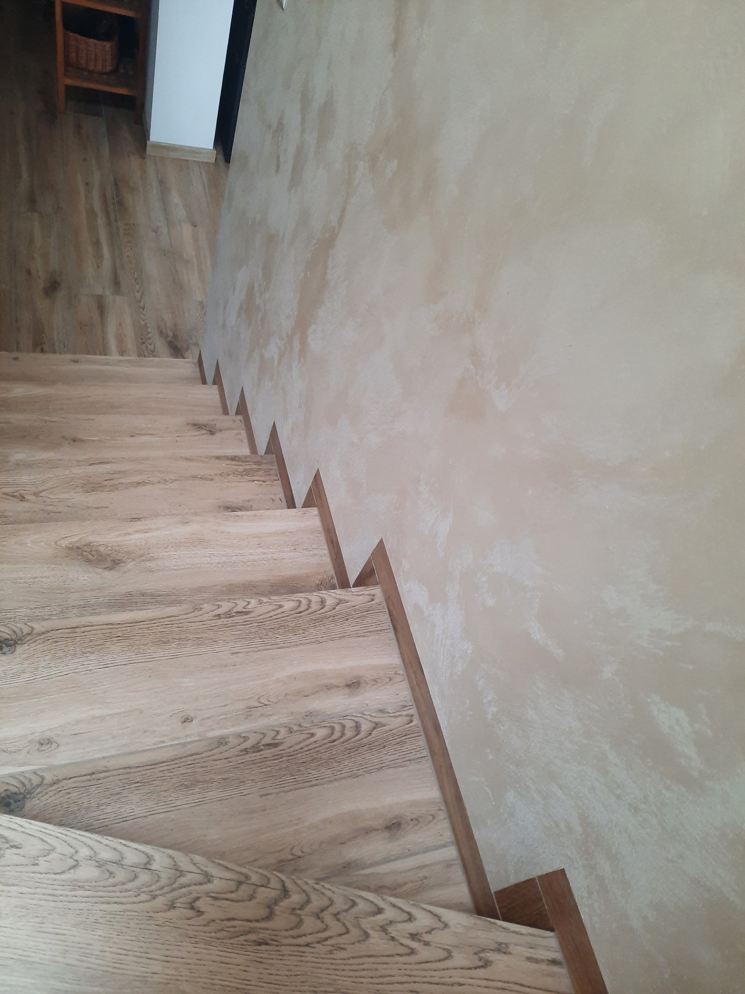 Drewnopodobne panele na schodach z wykończeniem przy ścianie o fakturze dekoracyjnej.