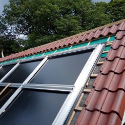 Dawid Romaniuk - Montaż paneli fotowoltaicznych na skośnym dachu pokrytym częściowo czerwoną dachówką w Złotoryi. Widoczne elementy konstrukcyjne i zabezpieczenie pod panelami.