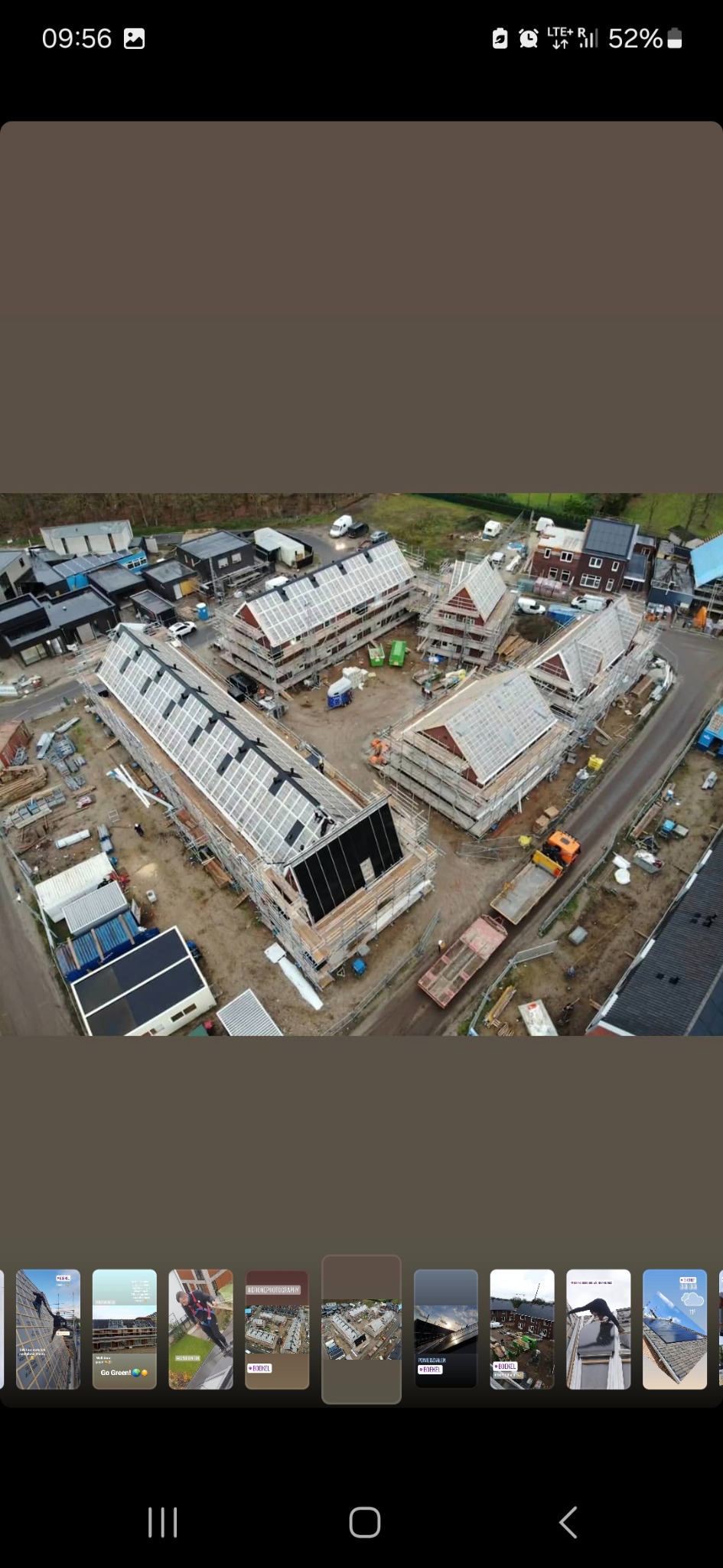 Widok z drona na plac budowy z kilkoma domami w trakcie krycia dachu panelami słonecznymi, otoczonymi rusztowaniami i sprzętem budowlanym.