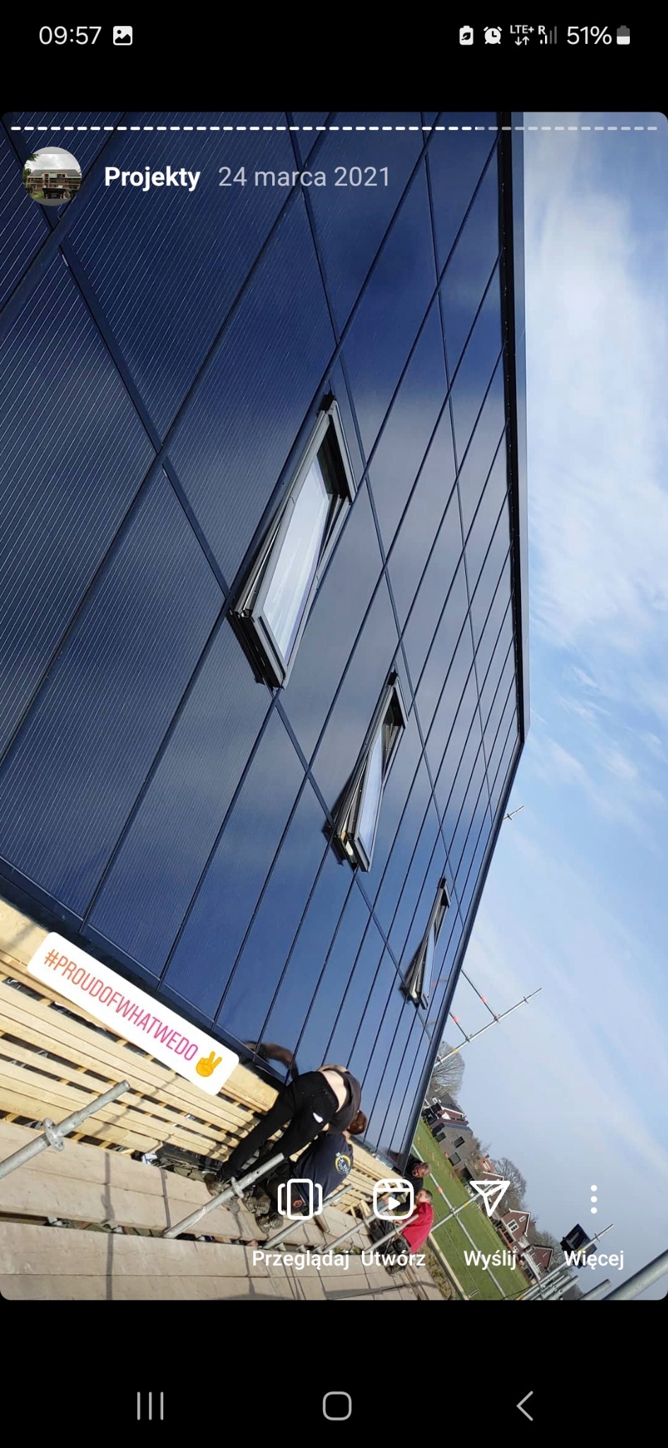 Elewacja budynku pokryta panelami, widoczne otwarte okna dachowe i pracownicy na rusztowaniu podczas montażu.