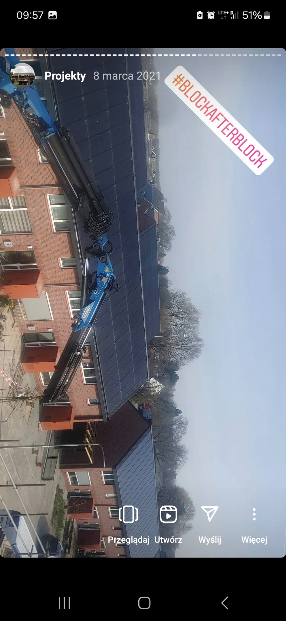 Montaż paneli fotowoltaicznych na dachu budynku mieszkalnego przy użyciu dźwigu. Widoczny fragment elewacji z cegły i okna. Na dachu zamontowane czarne panele.