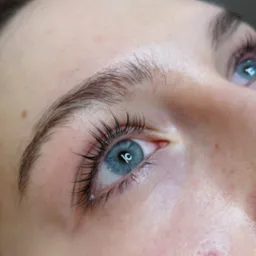 Zbliżenie na oko z niebieską tęcz&oacute;wką i świeżo podkręconymi, wydłużonymi rzęsami po zabiegu liftingu, widoczny delikatny błysk na rzęsach.