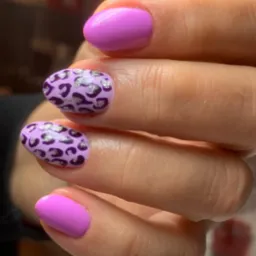 Zbliżenie dłoni z fioletowym manicure, dwa paznokcie w jednolitym kolorze, dwa w panterkę z brokatowymi akcentami.