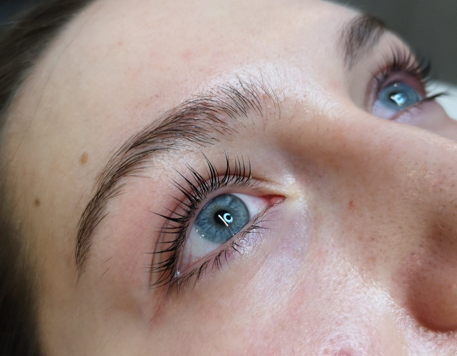 Zbliżenie na oko z niebieską tęczówką i świeżo podkręconymi, wydłużonymi rzęsami po zabiegu liftingu, widoczny delikatny błysk na rzęsach.