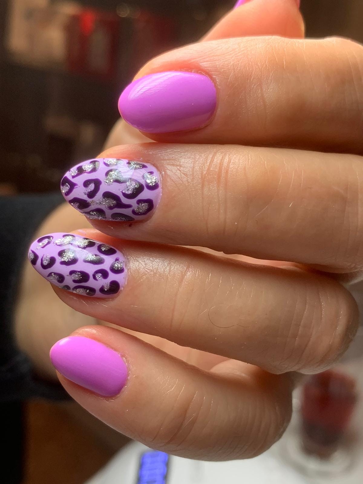 Zbliżenie dłoni z fioletowym manicure, dwa paznokcie w jednolitym kolorze, dwa w panterkę z brokatowymi akcentami.