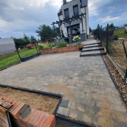 DAN-BUD Dawid Kępczyński - Ułożona kostka brukowa na podjeździe przed nowoczesnym domem z pergolą, widoczne obrzeża i przygotowane miejsce pod rabaty z cegły