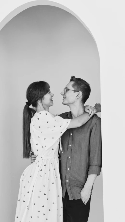Czarno-białe zdjęcie uśmiechniętej pary w objęciach, w łuku architektonicznym. Sesja w Warszawie. Sukienka w wisienki.