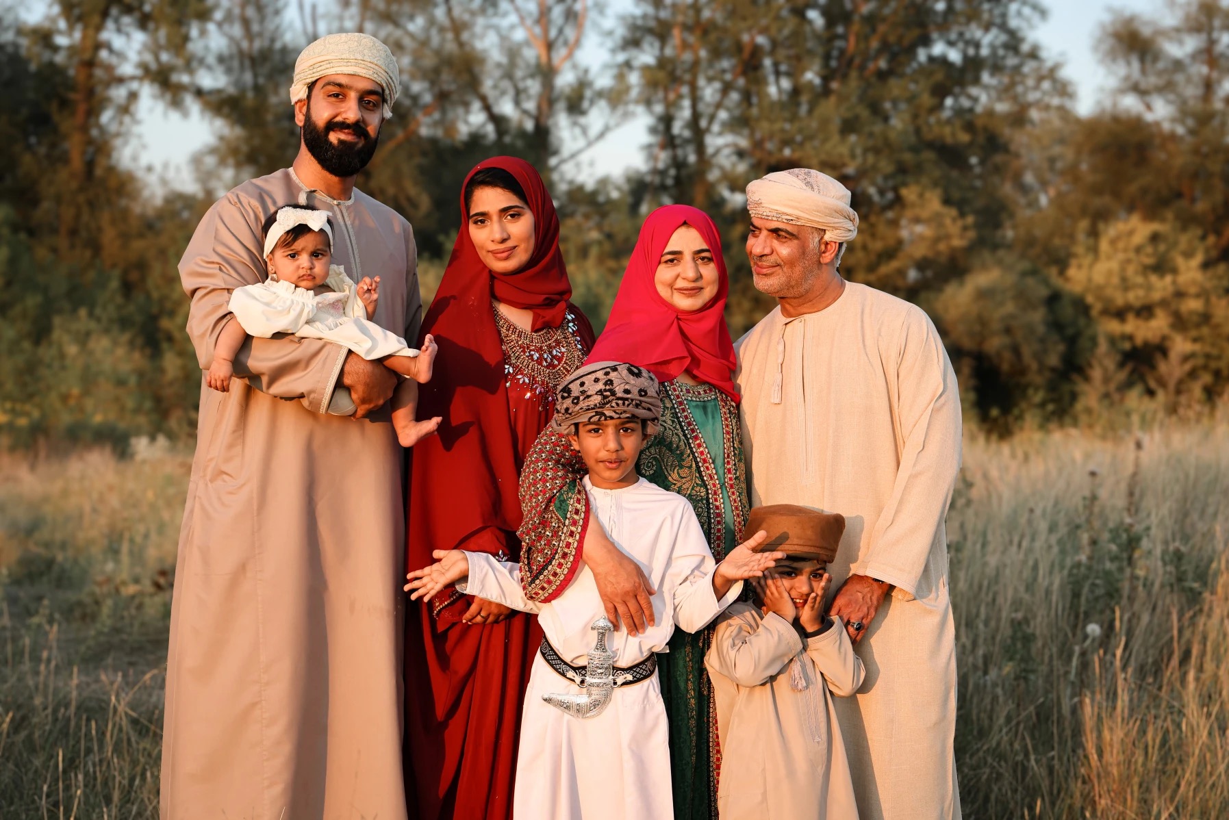 Portret rodzinny w tradycyjnych strojach omańskich na tle łąki o zachodzie słońca. Uśmiechnięci rodzice z dziećmi, ciepłe światło, naturalna sceneria.