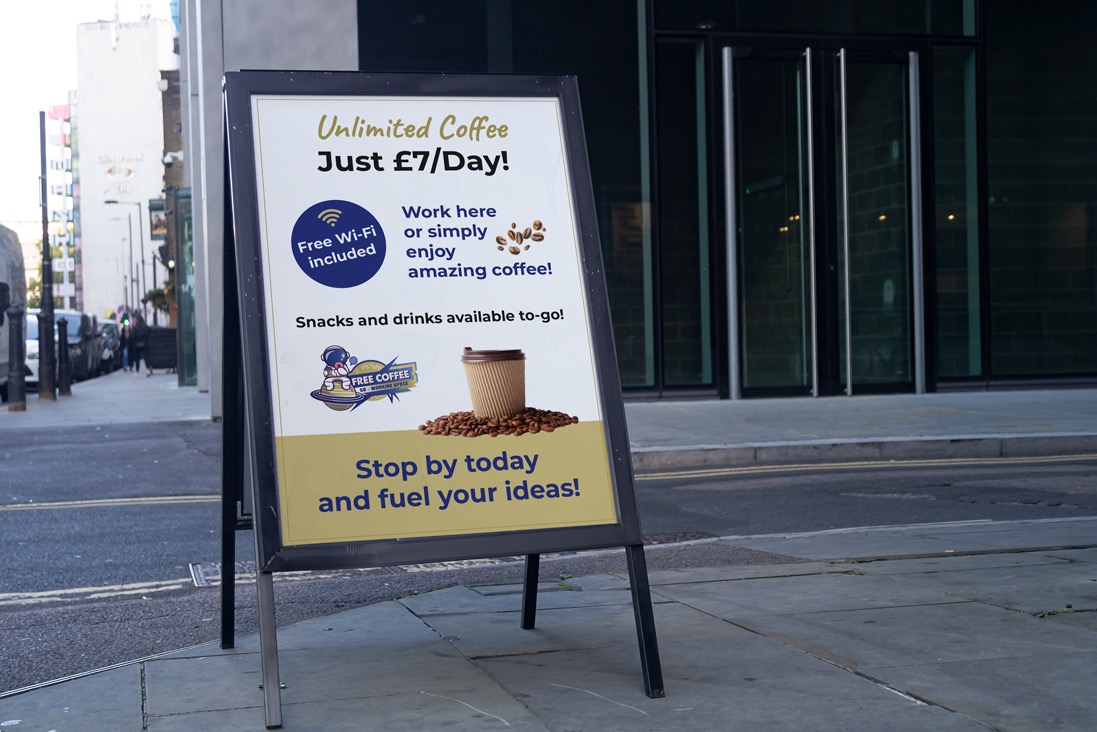 Potykacz reklamowy na chodniku przed budynkiem, z ofertą 'Unlimited Coffee Just £7/Day!' i logo 'Free Coffee Co-Working Space'.