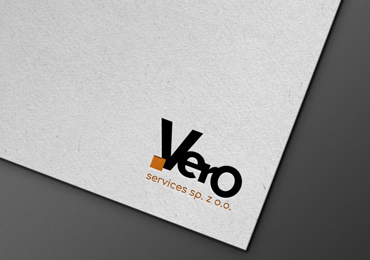 Logo 'Vero services sp. z o.o.' w czerni i pomarańczy na teksturowanym, białym tle, umieszczone na kartce leżącej ukośnie na szarym tle.