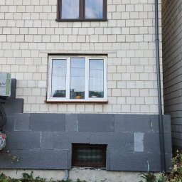 MADMART - Fragment elewacji budynku z oknami, częściowo ocieplony grafitowym styropianem, na balkonie paczka styropianu Mega Styro