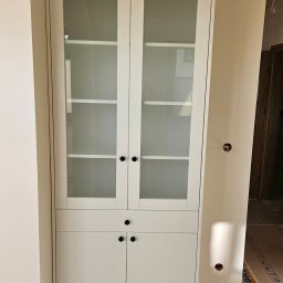 Bomax - Biała przeszklona szafa z szufladami i szafkami w trakcie montażu, widoczne niedokończone wykończenie ścian i instalacja elektryczna.