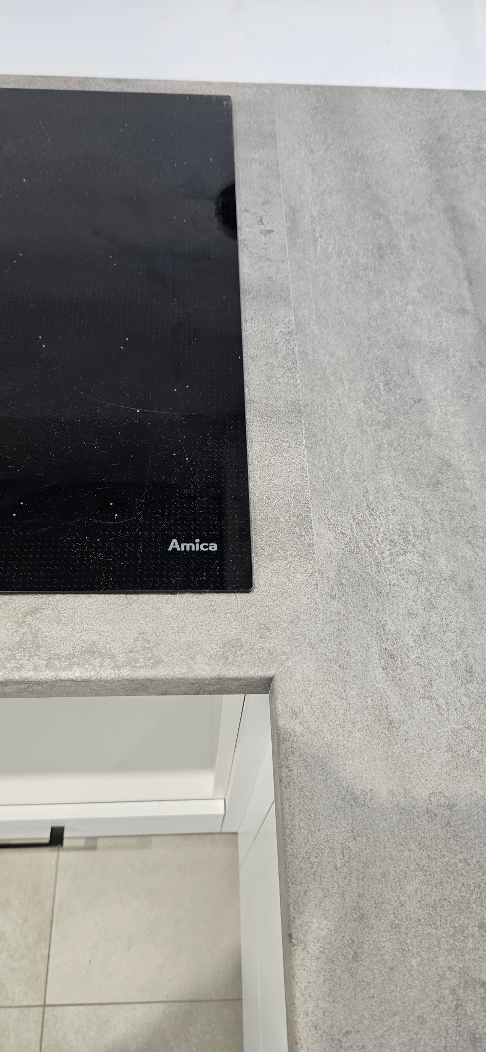 Fragment szarego blatu kuchennego z płytą indukcyjną marki Amica w Chełmku, widoczny fragment białej szafki pod zabudowę.