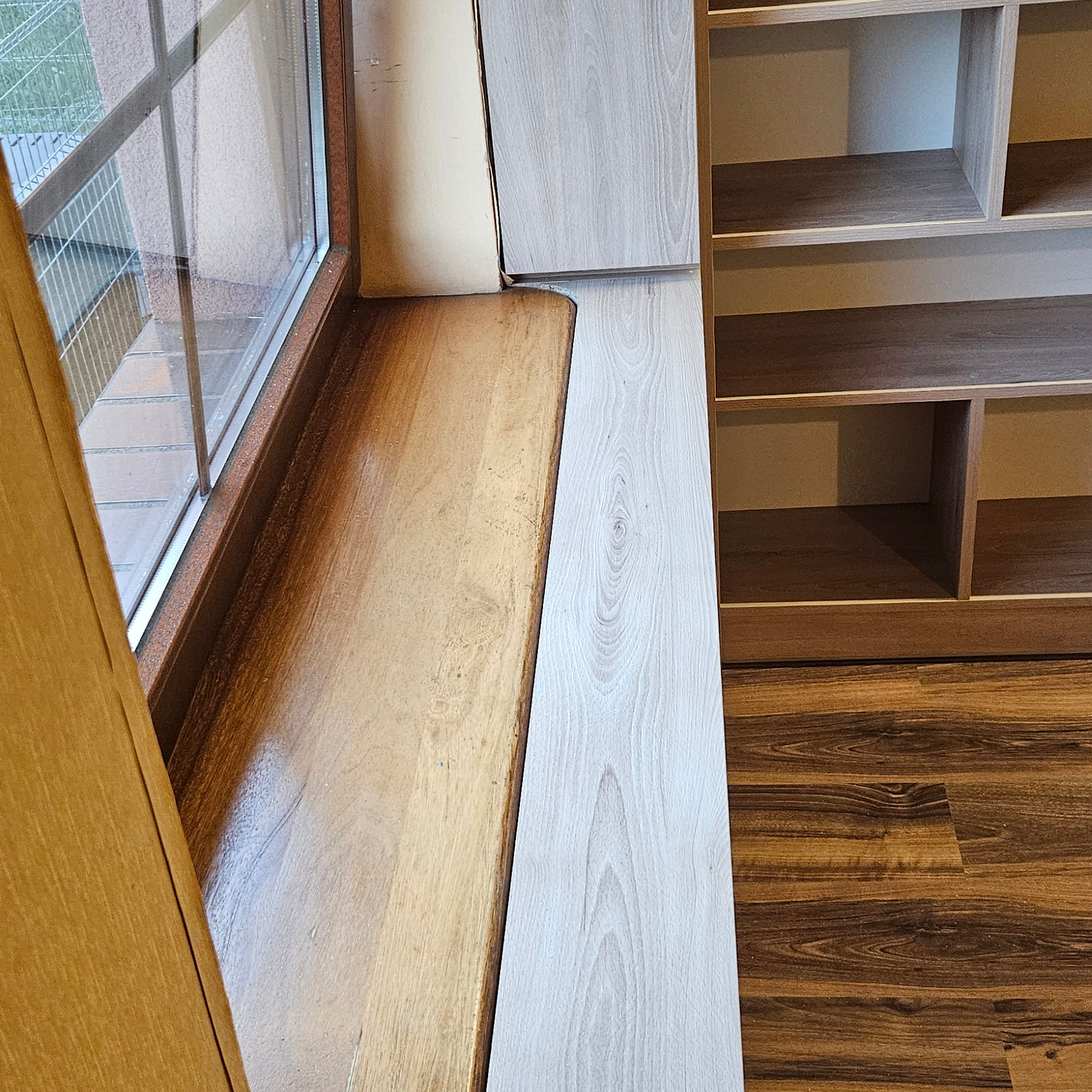 Drewniany parapet okienny sąsiadujący z szafką na wymiar z jasnego drewna i brązową podłogą.